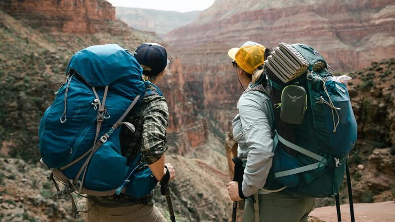 Hai du khách mang balo lớn trekking qua hẻm núi, minh họa sự khác biệt giữa du lịch tự túc và du lịch theo tour
