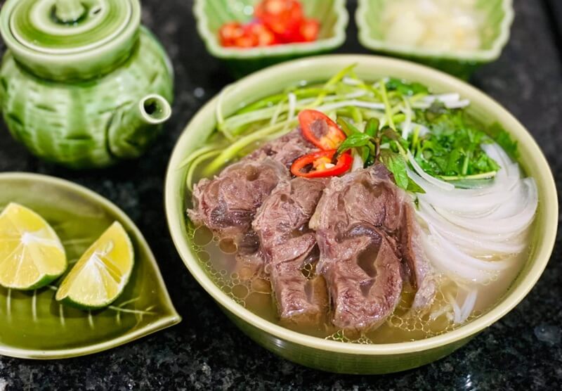 Phở bò Việt Nam với thịt bò, hành tây, rau thơm và chanh ớt ăn kèm