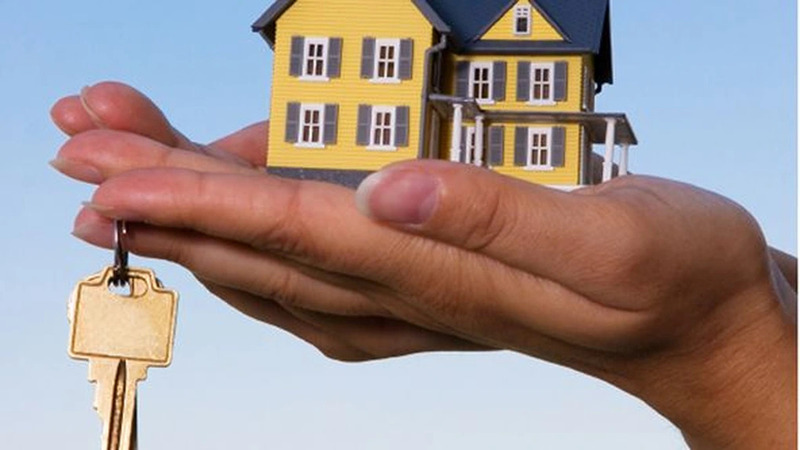 Bàn tay nâng mô hình ngôi nhà và chìa khóa, biểu tượng cho việc mua nhà và sở hữu tài sản