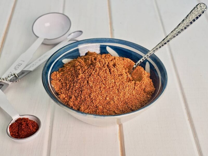 Bát bột Tandoori masala cùng muỗng đo lường, nổi bật với tông đỏ cam đặc trưng