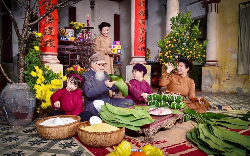 Gia đình quây quần gói bánh chưng, trang trí mai vàng và quất, thể hiện không khí Tết Nguyên đán truyền thống