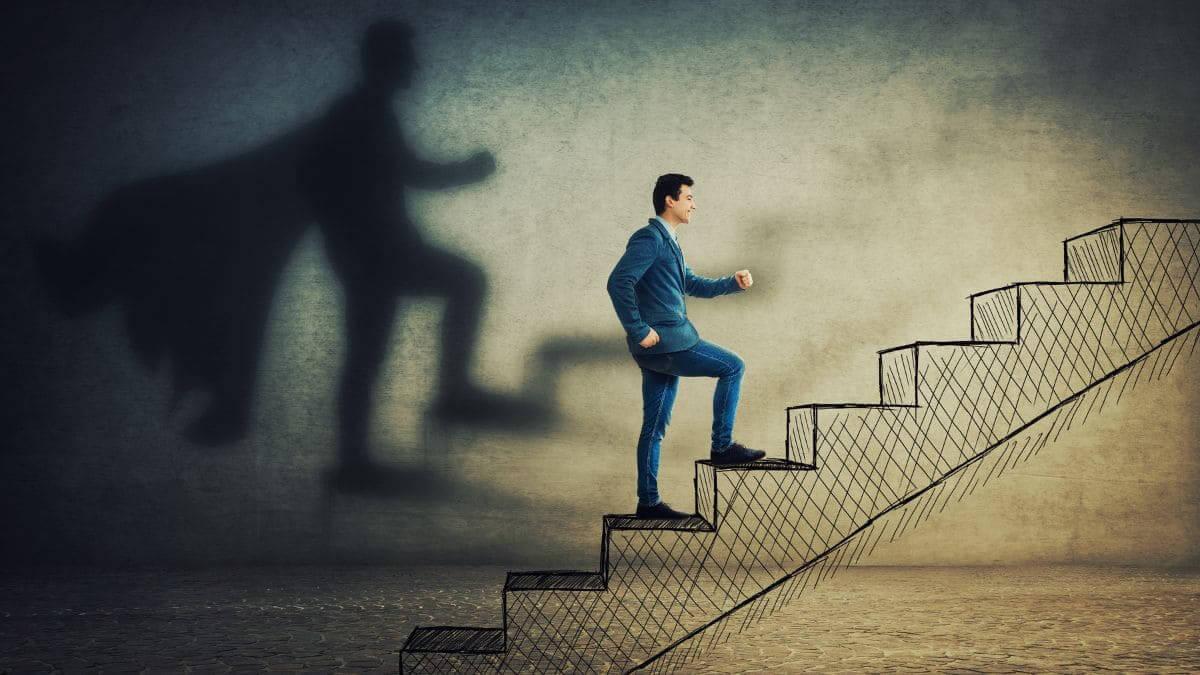 Người đàn ông bước lên cầu thang với bóng đổ thành siêu anh hùng, biểu tượng cho theo đuổi ước mơ