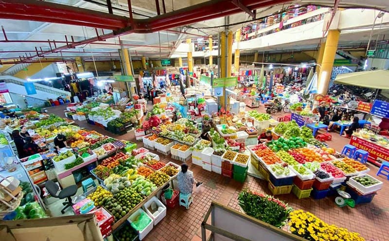 Gian hàng rau củ quả tại chợ truyền thống, với cảnh mua bán nhộn nhịp